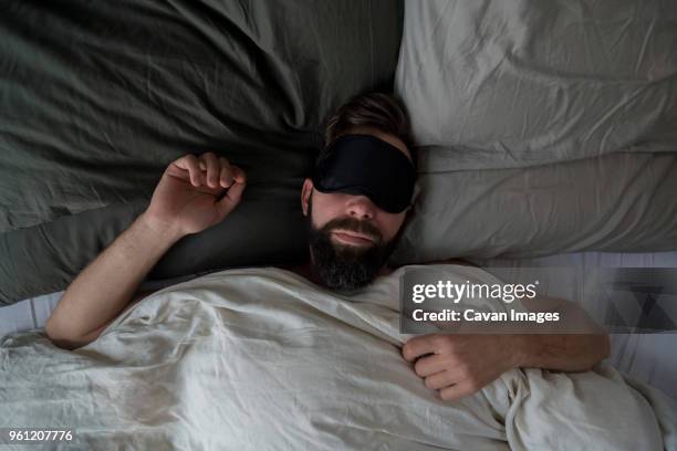 high angle view of man wearing sleep mask while sleeping on bed at home - masque pour les yeux photos et images de collection