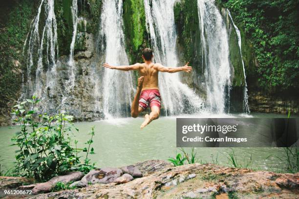 man jumping in river against waterfall - waterfall-jump stock pictures, royalty-free photos & images