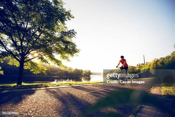 male cyclist on road by lake against clear sky - minneapolis park stock pictures, royalty-free photos & images