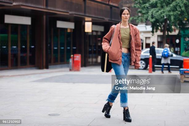 Model Runa Neuwirth wears a peach colored bomber jacket, green cropped tank top, blue jeans, and black heeled boots during London Fashion Week...