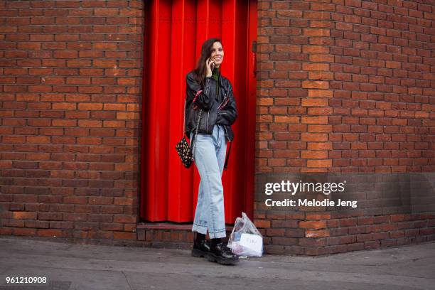 Model Ruby Aldridge talks on the phone and wears a black leather jacket, small black floral purse, blue jeans, and black chunky boots during London...