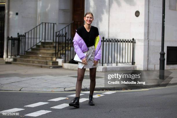 Model Vera Van Erp wears a purple puffer jacket off her shoulders, red top, skirt, tights, and black boots during London Fashion Week Spring/Summer...