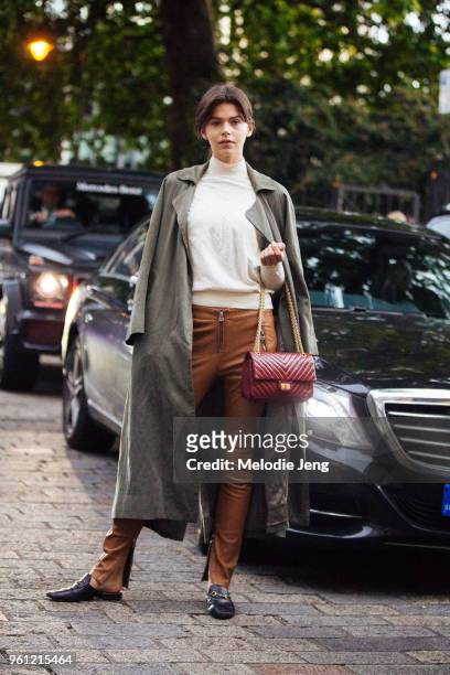 Model Georgia Fowler wears a long olive jacket, white top, light brown leather pants, red Chanel bag, and Gucci leather loafers during London Fashion...