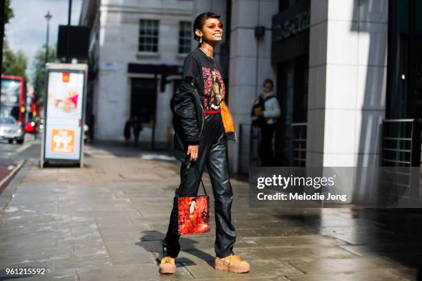 Model Theresa Hayes wears red sunglasses, a black bomber jacket off her shoulders, black graphic shirt, black leather pants, red graphic bag, and...