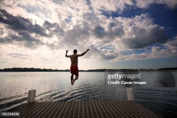 rear view of man jumping into lake against cloudy sky - minneapolis lake stock pictures, royalty-free photos & images