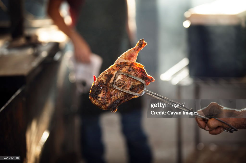 Cropped image of female chef holding chicken while coworker standing in background