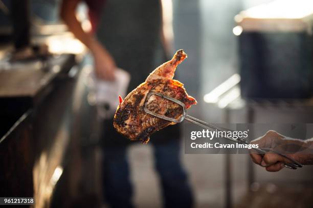 cropped image of female chef holding chicken while coworker standing in background - pinça utensílio de servir - fotografias e filmes do acervo
