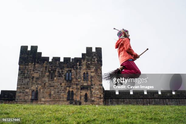 side view of girl jumping with broom against castle - englischesschloss stock-fotos und bilder