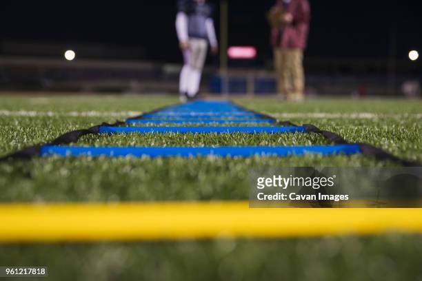agility ladder on grassy field at stadium with american football player and coach in background - agility ladder stock pictures, royalty-free photos & images