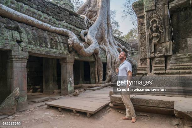 jonge man zwerven in de oude tempel van ta prohm in cambodja bewonderen van de structuur en de bomen groeien over - siem reap stockfoto's en -beelden