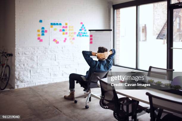businessman sitting on chair with hands behind head in creative office - office chair back fotografías e imágenes de stock