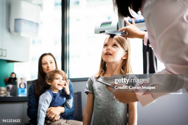 doctor measuring girls height while family sitting at clinic - pediatrician bildbanksfoton och bilder