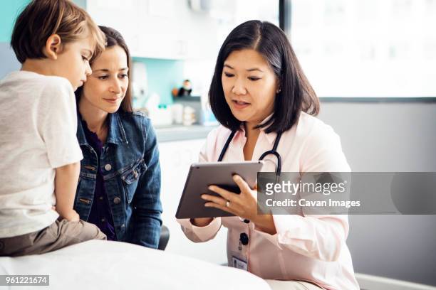 doctor explaining report on tablet computer to family in clinic - screening of netflixs to all the boys ive loved before arrivals stockfoto's en -beelden