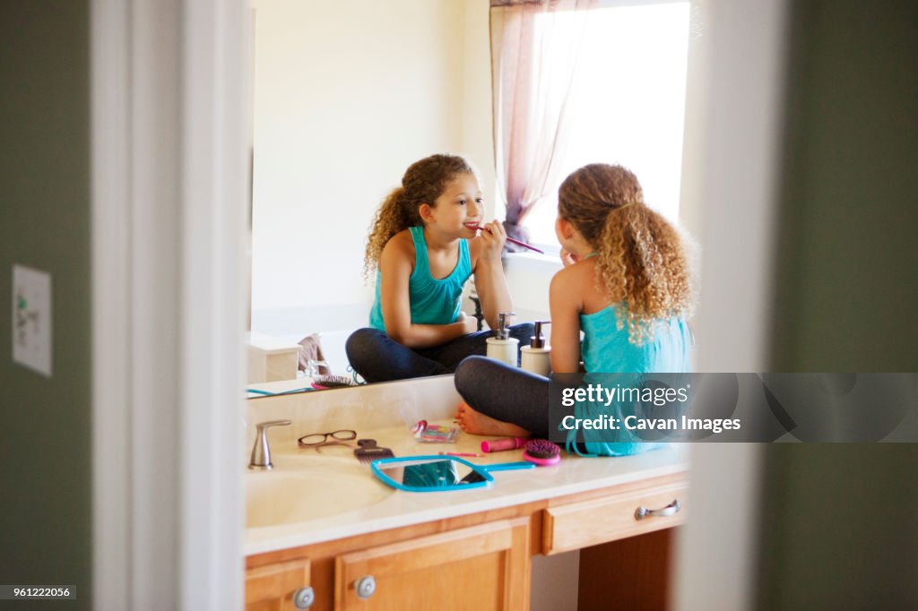 Girl applying make-up in mirror at home