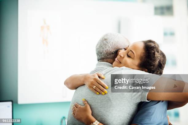 side view of female doctor embracing senior male patient in clinic - embracing stock pictures, royalty-free photos & images