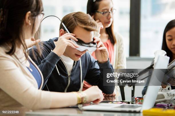 male student wearing virtual reality glasses while sitting by friends in classroom - male teacher in a classroom stock-fotos und bilder