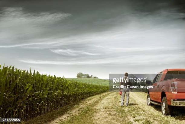 rear view of farmer standing by car on field against cloudy sky - autobauer stock-fotos und bilder