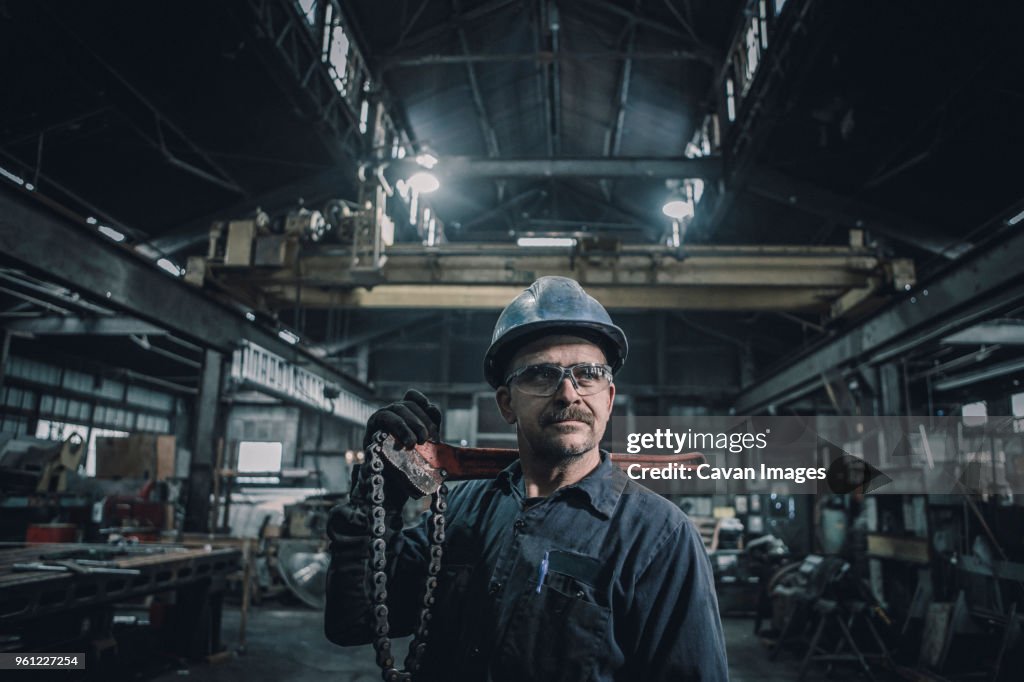 Male worker carrying work tool looking away while standing in factory