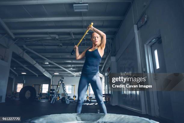 woman hitting tire with sledgehammer while training at gym - sledgehammer stockfoto's en -beelden