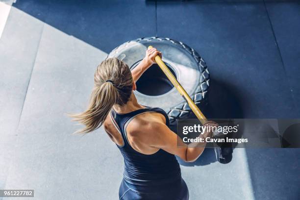 high angle view of woman hammering tire while exercising in gym - sledgehammer stockfoto's en -beelden