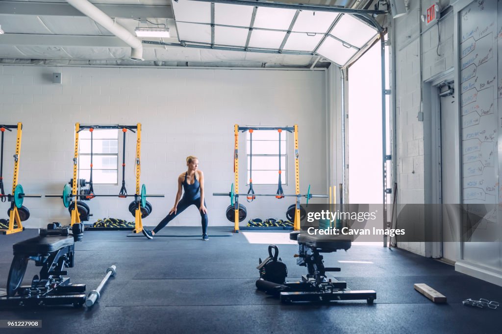 Young woman stretching legs against wall in health club