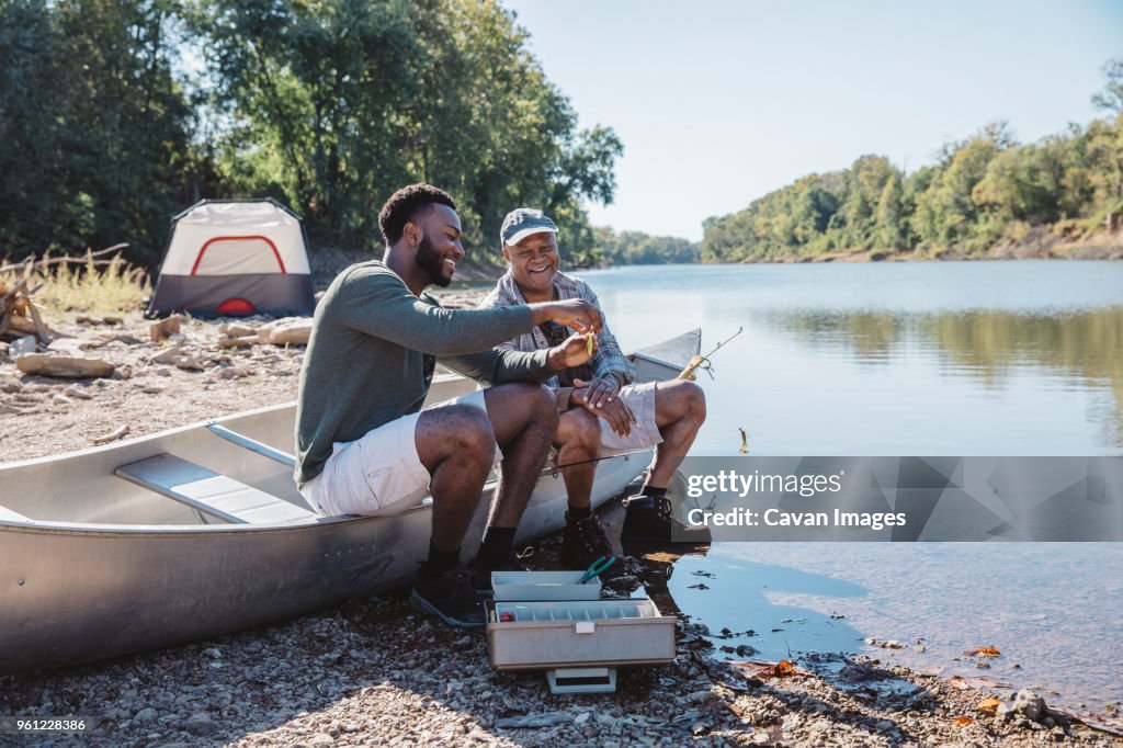 Happy male friends adjusting fishing tackle on boat at lakeshore