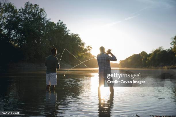 rear view of male friends fishing while standing in lake against sky - an evening for mo and friends stockfoto's en -beelden