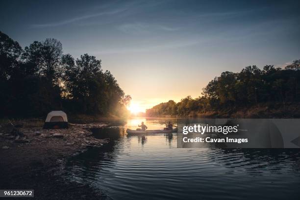 silhouette male friends rowing on lake against sky during sunset - missouri lake stock pictures, royalty-free photos & images