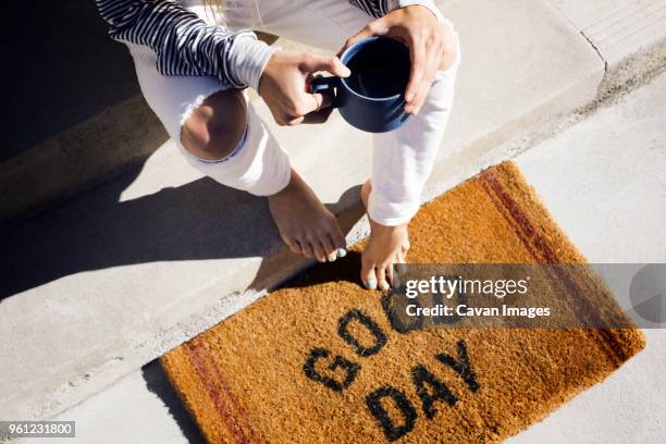 overhead view of woman holding coffee cup while sitting on steps at entrance - welcome mat stock pictures, royalty-free photos & images