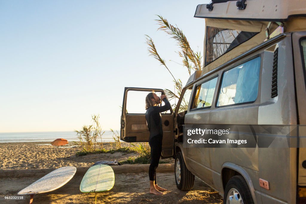 Side view of male surfer having drink outside mini van on San Onofre State Beach
