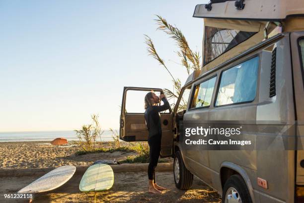 side view of male surfer having drink outside mini van on san onofre state beach - wetsuit stock pictures, royalty-free photos & images