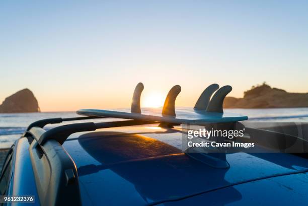 surfboard on car roof at beach against clear sky during sunset - tillamook county stock-fotos und bilder