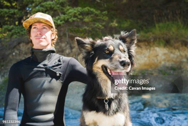 man looking away while relaxing with dog at beach - neoprenanzug stock-fotos und bilder