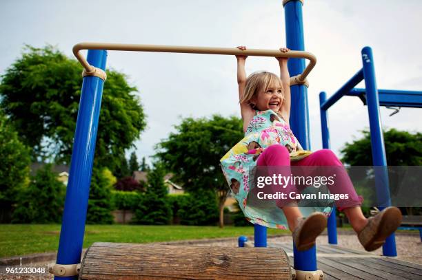 cheerful girl hanging on monkey bars in park - playground equipment stock pictures, royalty-free photos & images