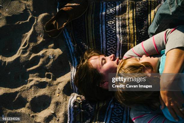 overhead view of woman embracing daughter while lying on beach towel - woman towel beach stockfoto's en -beelden