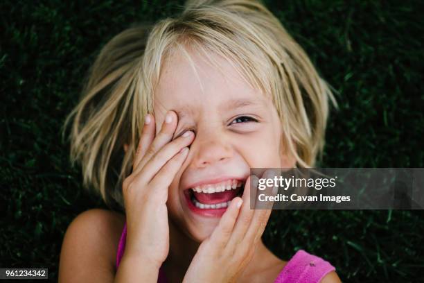 overhead portrait of happy girl rubbing eye while lying on grass - child eyes stock-fotos und bilder