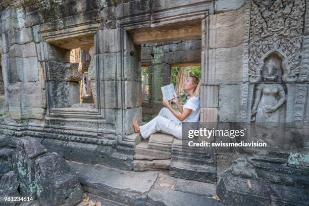 friendly beautiful female traveler holding guidebook reading travel informations on the angkor wat complex ancient temples in cambodia - blonde hair roots stock pictures, royalty-free photos & images