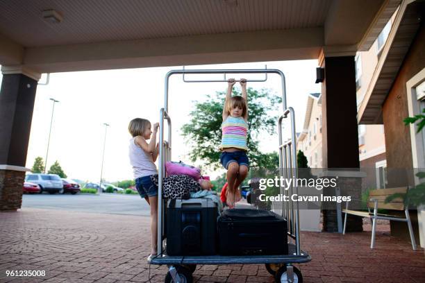 sisters playing on luggage cart outside hotel - luggage trolley stock pictures, royalty-free photos & images