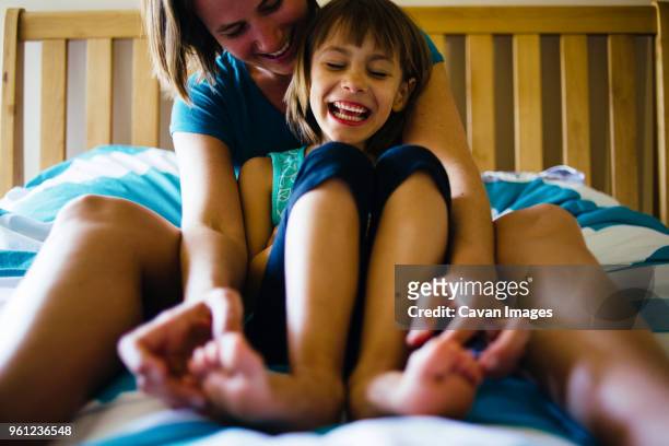 happy mother tickling daughters feet while sitting on bed - happy feet stockfoto's en -beelden