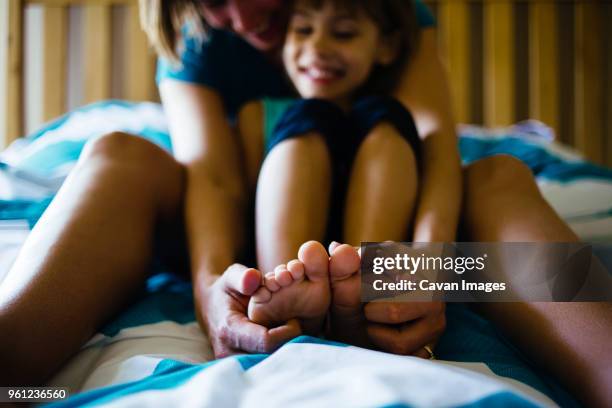 mother tickling daughters feet while sitting on bed at home - tickling feet - fotografias e filmes do acervo