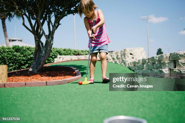 girl playing miniature golf during sunny day - minigolf foto e immagini stock