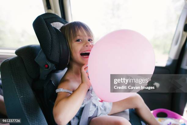 portrait of happy girl playing with balloon while sitting in car - repose tête photos et images de collection