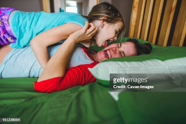 side view of playful daughter licking mothers cheek on bed at home - cheek tongue stock pictures, royalty-free photos & images