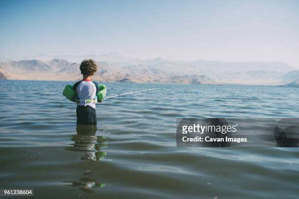 rear view of boy fishing while standing in river against clear sky during sunny day - kernville stock pictures, royalty-free photos & images
