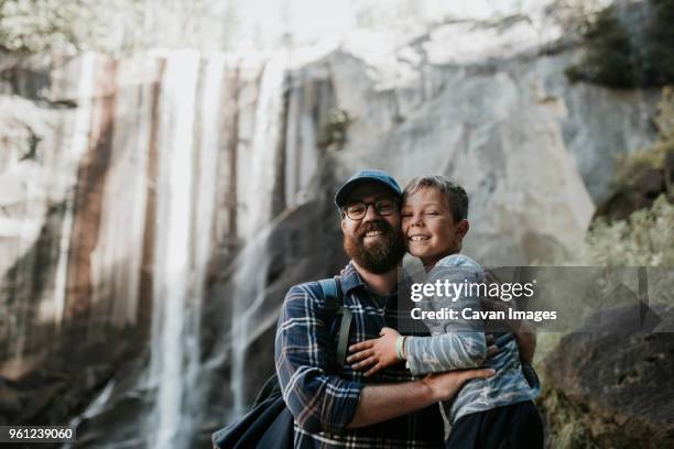 portrait of cheerful father and son against waterfall at yosemite national park - mann bart portrait mit kind stock-fotos und bilder