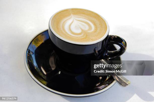 a flat white milk coffee in a black cup and saucer on a white table at a sidewalk cafe - black milk australia stock pictures, royalty-free photos & images