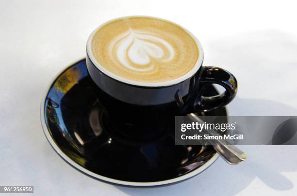 a flat white milk coffee in a black cup and saucer on a white table at a sidewalk cafe - black milk australia stock pictures, royalty-free photos & images