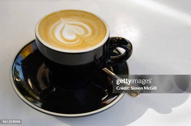 a flat white milk coffee in a black cup and saucer on a white table at a sidewalk cafe - black milk australia stock pictures, royalty-free photos & images