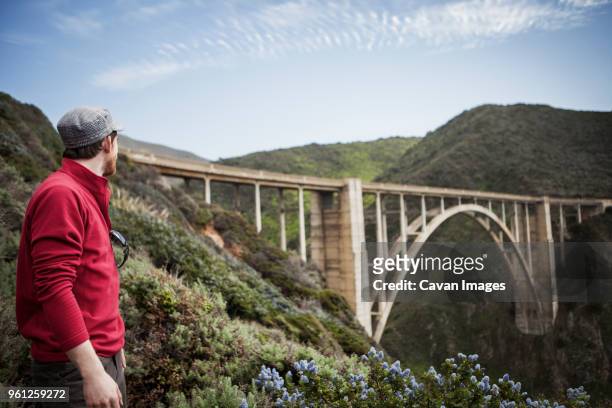 male hiker looking at bixby creek bridge - bixby bridge stock-fotos und bilder