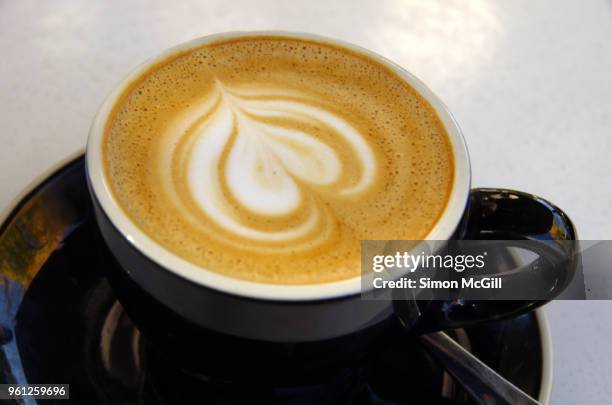 a flat white milk coffee in a black cup and saucer on a white table at a sidewalk cafe - black milk australia stock pictures, royalty-free photos & images